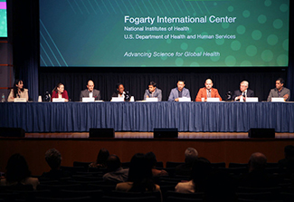 Alumni and NIH moderators sit at a table on the stage of the Natcher Center at NIH.