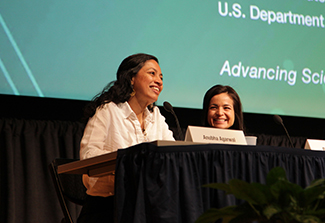 This photo shows Anubha Agarwal (left) speaking  during the Fogarty Global Health Fellows & Scholars 20th Anniversary event as Roxanna Garcia(right) looks on. Both women are seated at a table and are smiling.