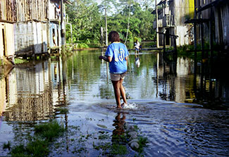 Woman walks through flooded street, water up to her ankles, 2-story wooden buildings on either side of street