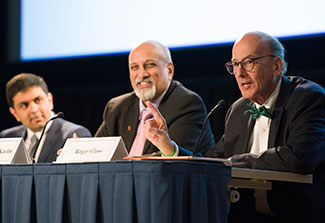 Vivek Naranbhai, Salim Abdool Karim and Roger Glass seated, speaking at panel table in auditorium