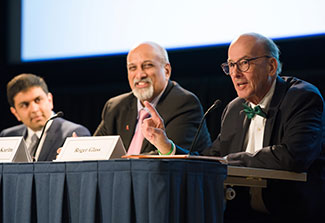 Vivek Naranbhai, Salim Abdool Karim and Roger Glass seated, speaking at panel table in auditorium