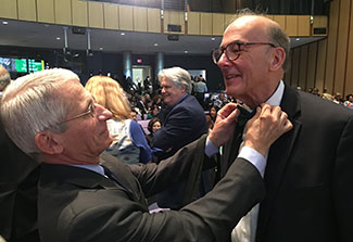 Tony Fauci straightens Roger Glass’s bowtie in the audience of the auditorium