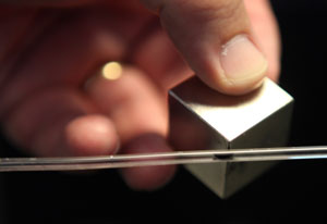 Close up of hand dragging square magnet along thin clear plastic tube, liquid in tube is attracted by the magnet