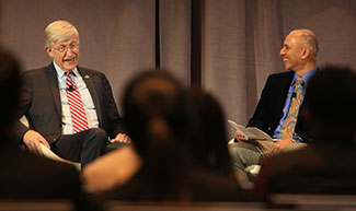 NIH Director Dr. Francis S. Collins and ASTMH President Dr. Chandy John speak together, seated in front of an audience.