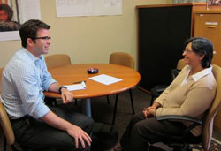 Benjamin Bearnot seated at table in office across from Dr. Quarraisha Abdool Karimsaid, they look at each other