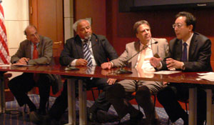 Dr Roger Glass, Ambassador Eric Goosby and two men, all in suits, seated at panel table with microphones in conference room