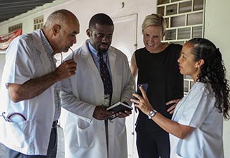 Bill Pape reviews information on a mobile device with three researchers in a hallway