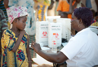 Young girl rolls up sleeve preparing to receive vaccination in arm from health care worker at busy outdoor clinic