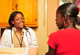 Woman medical worker in white coat with stethoscope around neck smiles and listens to woman patient in profile