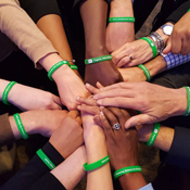 Hands join in the middle of a huddle pictured from above, all wearing bright green Fogarty wristbands