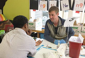 Healthcare worker sits across from health fair participant, testing supplies on the table between them.