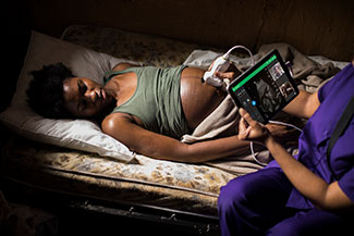 Medical worker performs ultrasound connected to a table on a pregnant woman lying on cot.