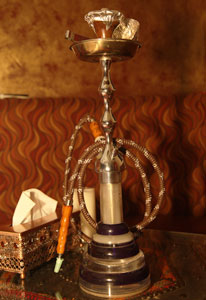 Waterpipe sits on top of an empty table in a hookah bar, hose coiled neatly.
