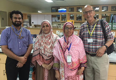 In research lab one male and two female trainees pose with Fogarty Director Dr. Roger Glass