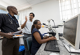 Dr. Satish Gopal talks with UNC-Project Cancer Program staff Tamiwe Tomoka (at microscope) and Edwards Kasonkanji (standing).