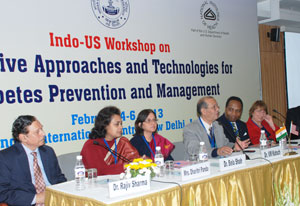 Three men and three women sit at conference panel table, sign with NIH logo in background reads Indo-US Workshop 