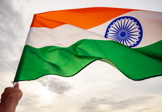 This photo shows an Indian flag being waved by a person’s hand against the sky