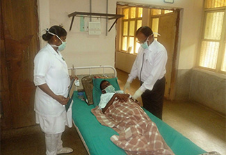 Two Indian medical staff care (standing) for a patient (lying in a hospital bed) with multi-drug resistant tuberculosis. All are wearing masks.