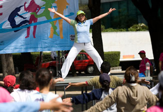 A female instructor on stage leads a large, outdoor exercise class