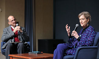 Dr. Jody Olsen speaks into a miscrophone on stage, seated with Dr. Roger Glass.