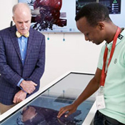 In this photo, a student (right) demonstrates the use an “Anatomage” table - a 3D anatomy visualization and virtual dissection tool for anatomy and physiology education - while Acting Fogarty Director Peter Kilmarx (left) looks on.