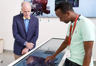 In this photo, a student (right) demonstrates the use an “Anatomage” table - a 3D anatomy visualization and virtual dissection tool for anatomy and physiology education - while Acting Fogarty Director Peter Kilmarx (left) looks on.