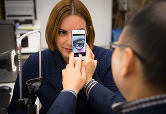 In this photo, Young Kim (foreground with his back to the camera)  uses a smart phone to take a photo of a woman’s inner eyelid. 