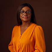 In this photo, Dr. Lola Kola wears an orange blouse as she faces the camera for a close-up shot.