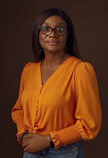 In this photo, Dr. Lola Kola wears an orange blouse as she faces the camera for a close-up shot.  