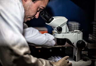 Constantinos Kurt Wibmer, wearing a white lab coat, peers into a microscope to look at protein crystals.