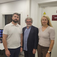 Three scientists stand facing the camera in a Kyiv radiology clinic. From left to right, Ukrainian scientist, Dr. Oleksiy Omelchenko, wears a tan shirt and dark slacks, Dr. Israel Liberzon wears a navy suit over an open-neck blue shirt and Dr. Tetiana Nickelsen wears a beige blouse over tan slacks.