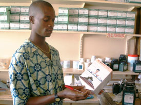 Healthcare worker examines large package of drugs, pharmaceutical shelves with similar packages, pill bottles in background