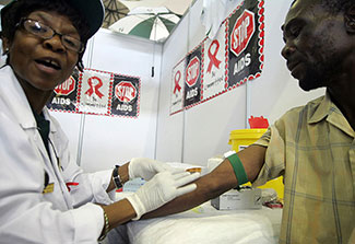 Female health worker performs a blood test on a man, stop AIDS posters on the wall.