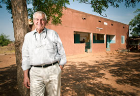 Dr Marc LaForce leans against a tree in the shade in front of a health clinic in Africa