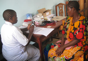 Woman medical worker enters data on smartphone while seated across table from a female patient