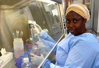 Dr. Djeneba Dabitao, dressed in blue scrubs, reviews samples in a lab.