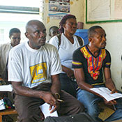 A group of men and women in Liberia sitting on wooden benches in a classroom during a training session to improve understanding of mental disorders.