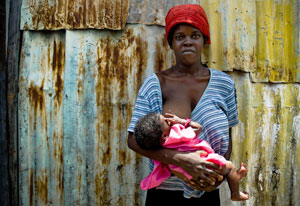 Woman stands while nursing a baby, solemn frown on her face