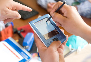 Close up of hands using a hand-held electronic device to enter data using a stylus, other hands point to show instructions