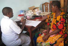 Woman medical worker enters data on smartphone while seated across table from a female patient
