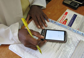Close up of smartphone sitting on top of papers, hands hold pen while entering data