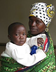 Mother wearing bright shall and head wrap over hear holds an infant in her arms, both look at camera