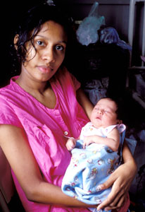 Woman looks directly at camera, holds a small baby wrapped in a blanket