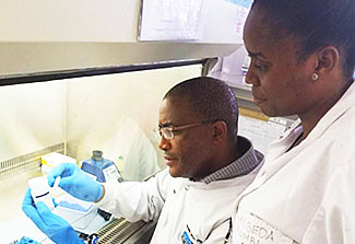 Dr. Moyo Sikhulile and a colleague dressed in lab coats work with sample in the lab