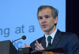 Dr. Christopher Murray speaks at a podium, slide projected in the background