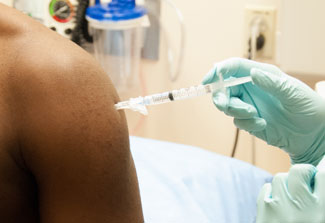 close up of health care worker wearing gloves giving patient a shot in the upper arm