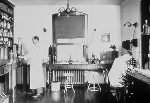 Black and white photo of two scientist in lab coats working in a laboratory in the 1880’s.