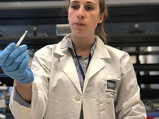 NIH investigator works in lab, holds swab tester.