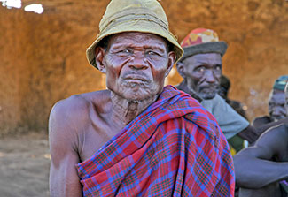 Elderly African man seated outside looks directly at camera