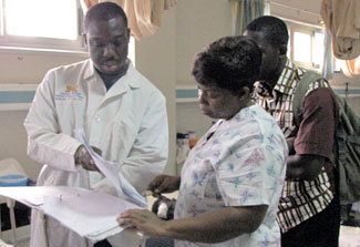 Dr Rockafeller Oteng examines a chart with others beside a hospital bed